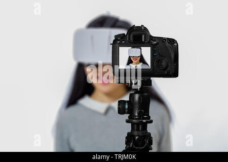 Focus sulla visualizzazione live su telecamera sul cavalletto, ragazza adolescente utilizzando occhiali VR immagine sul retro schermo con scena sfocata in background. Teenage livestre vlogger Foto Stock