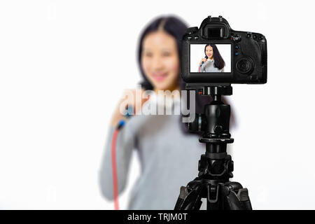 Focus sulla visualizzazione live su telecamera sul cavalletto, ragazza adolescente cantando con microfono immagine sul retro schermo con scena sfocata in background. Teenage vlogger l Foto Stock