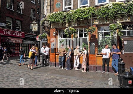 La folla di persone in piedi a bere pinte di birra al di fuori del Blue Posts pub di Berwick Street, Soho a Londra England Regno Unito KATHY DEWITT Foto Stock