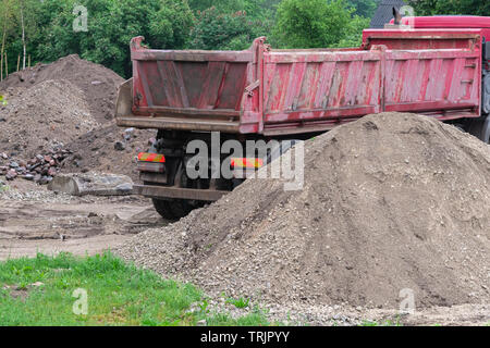 Grande autocarro pesante accanto a cumuli di terra, lo sviluppo urbano. Pesante macchina industriale all'aperto accanto alla sporcizia di pile, sito in costruzione Foto Stock