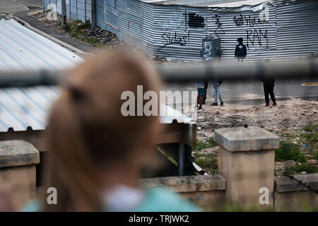 Ragazza giovane guardando i bambini che giocano in strada in una township in Africa da tutta una recinzione. Foto Stock