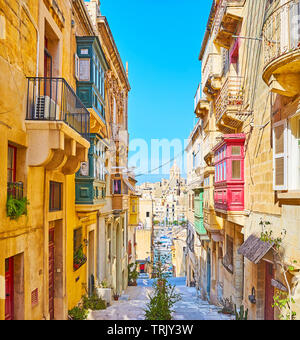 Il tipico paesaggio di Senglea con basse case residenziali, strade collinari, piante in vaso e Vittoriosa marina sullo sfondo, Malta. Foto Stock