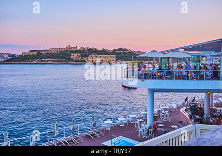 SLIEMA, Malta - 19 giugno 2018: affollato aperto terrazza del ristorante costiere su Tigne Point penisola con vista sulla valletta Porto settentrionale Foto Stock