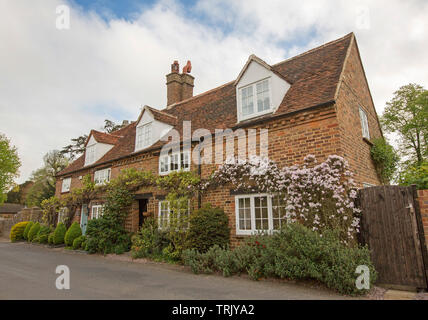 Edificio di due piani casa in mattoni rossi con finestre dormer con la clematide blooming sulle pareti e il giardino di arbusti nel villaggio di Denham, Buckinghamshire Inghilterra Foto Stock