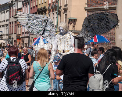 Busker / Street performer vestito come un angelo con un enorme ali, folla intorno a lui in attesa di scattare le foto. Musicista di strada, strada di esecuzione Foto Stock