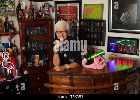 Attraente donna senior dietro il bar nel suo al-home bar, USA, 2018 © Katharine Andriotis Foto Stock