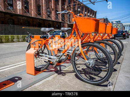 Grande strada arancione trasporto biciclette con cestello per merci per viaggiare intorno alla città di stand in fila sulla rete di noleggio parcheggio in attesa di Foto Stock