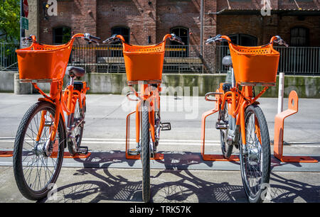 Grande strada arancione trasporto biciclette con cestello per merci per viaggiare intorno alla città di stand in fila sulla rete di noleggio parcheggio in attesa di Foto Stock