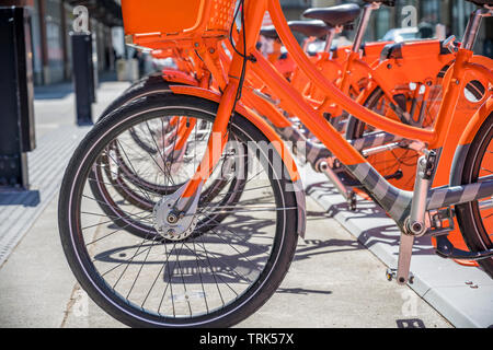 Via trasporto pubblico arancione noleggiare biciclette con cestello per viaggiare intorno alla città di stand in fila sulla rete di noleggio parcheggio in attesa di cyc Foto Stock