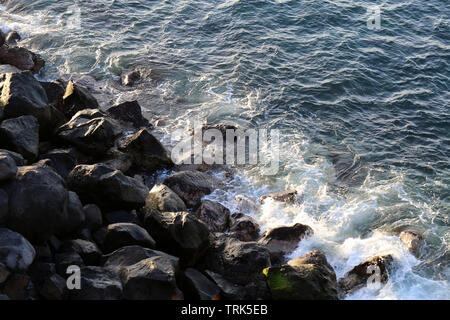 Piccole onde di colpire le rocce in una spiaggia situata a Madeira, Portogallo. La foto è stata scattata sotto la luce naturale durante una bella mattina di primavera. Foto Stock