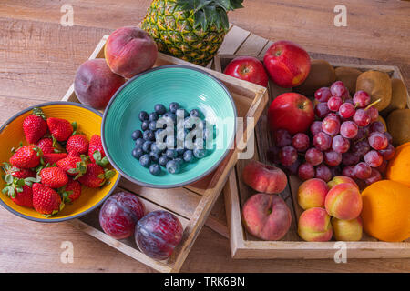 Due scatole piene di frutti colorati su un sfondo di legno. Contiene ananas, uva, mele, kiwi, arance albicocche, mirtilli e fragole. Foto Stock