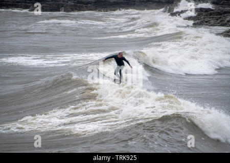 Surfista cavalcando le onde costiere durante le sessioni di surf in acqua fredda in una giornata coperta. Foto Stock
