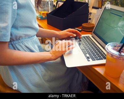 Bellissima gara di misto donna seduta in una caffetteria e sorridenti mentre si utilizza il suo computer portatile Foto Stock