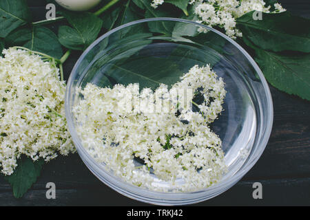 Fiori bianchi e foglie di sambuco giacciono su una ciotola su un rustico sfondo di legno. I fiori di Sambucus specie sono utilizzati per produrre lâ Elderflower co Foto Stock