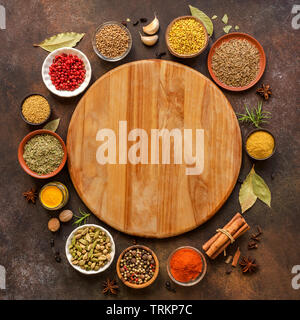 Varie spezie in legno scuro dello sfondo. Assortimento, set di spezie e condimenti con tagliere, vista dall'alto, copia dello spazio. La cottura di alimenti del concetto. Foto Stock