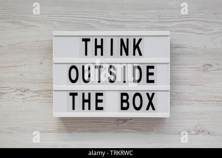 "Pensare al di fuori della casella di parole su un lightbox su un bianco superficie in legno, vista dall'alto. Piatto, laici overhead, dall'alto. Close-up. Foto Stock