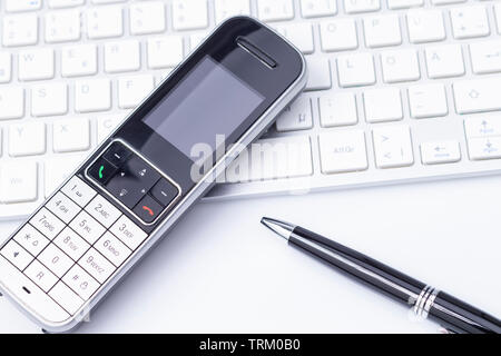 L'immagine mostra un telefono su una tastiera con una penna isolato su bianco Foto Stock