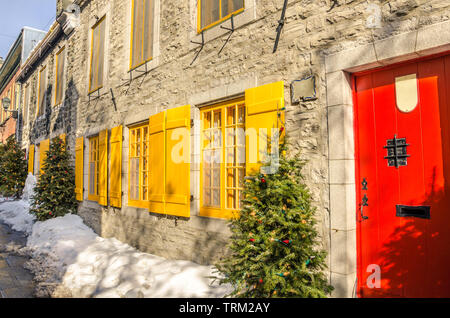 Antica pietra huose con un rosso di legno porta anteriore e persiane di colore giallo su una soleggiata giornata invernale Foto Stock