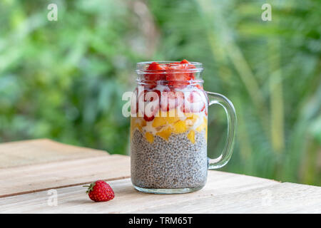 Latte di Mandorla chia pudding con fragole fresche e mango in un vasetto di vetro mug. Vegan materie prima colazione. Semi di Chia e taglio freschi frutti e bacche desser Foto Stock