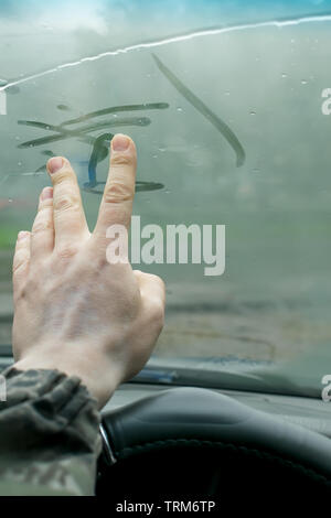La mano umana le dita le linee di disegno su un sudato umidità dall'interno di vetro dell'auto in condizioni di tempo piovoso Foto Stock