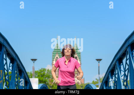 Basso angolo vista di una donna sorridente jogging attraverso un arco ponte urbano Foto Stock