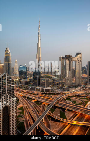 Il Burj Khalifa e il centro cittadino di Dubai che includono un massiccio interscambio autostradale al tramonto Foto Stock