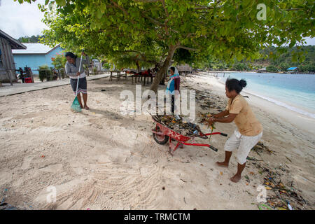 Isola di Papua gli abitanti di un villaggio di clearing fino in plastica rifiuti marino oggetto di dumping sulla spiaggia in Manyaifun durante una giornata di vento sulla isola di Batang Pele, West Wa Foto Stock