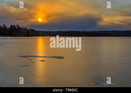 Bellissima alba con drammatica nuvoloso Nuvoloso cielo arancione su ghiaccio congelato coperto Lago Uspen in Svezia Foto Stock