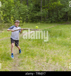 Giovane ragazzo a giocare a baseball o macchine versatili colpendo palla da tennis con bastone di legno Foto Stock