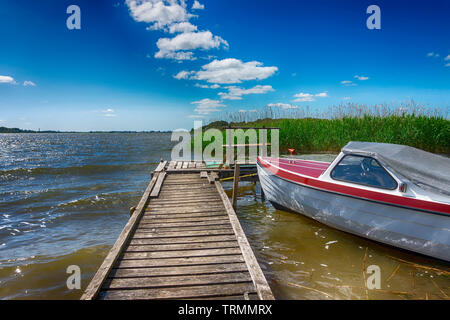 Piccolo motoscafo ormeggiato al fianco di un molo di legno in un lago ruvida con piccole onde in una vista sfuggente lungo la passerella Foto Stock