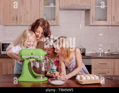 La grande famiglia - una madre e tre bambini - due figlie ed un figlio, cuoco in cucina, montare la panna in un frullatore. Messa a fuoco selettiva. Foto Stock