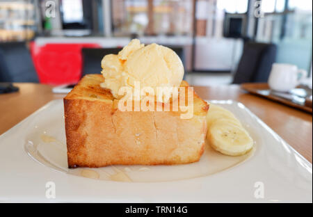 Pane dolce miele santos gelato alla vaniglia con panna montata banana di frutta e miele delle api su piastra bianca nella caffetteria cafe Foto Stock