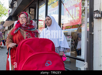 Due donne musulmane in hijabs, probabilmente sorelle, a piedi verso il basso 74a san in Jackson Heights spingendo in rosso di un passeggino. Queens, NYC. Foto Stock