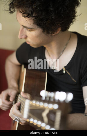 Giovane uomo suona la chitarra su un divano Foto Stock