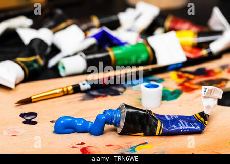 Una ripresa macro di un grande blob di vernice acrilica blu spremuto fuori di un tubo su una tavolozza di legno. Il tubo e il blob sono in una messa a fuoco nitida in avanti Foto Stock