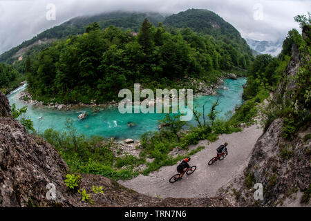 Due uomini ride mountain bike su un sentiero accanto alle acque turchesi del fiume Isonzo in Slovenia. Foto Stock