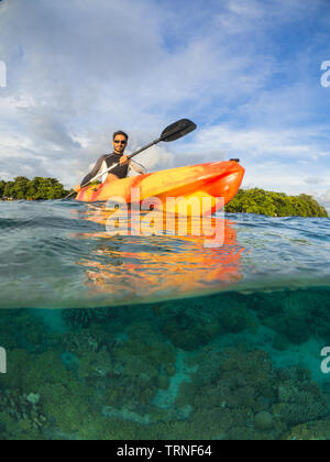 L'uomo kayak da un'isola al di sopra di una colorata barriera corallina sott'acqua nel Bunaken Marine Park, Nord Sulawesi, Indonesia Foto Stock