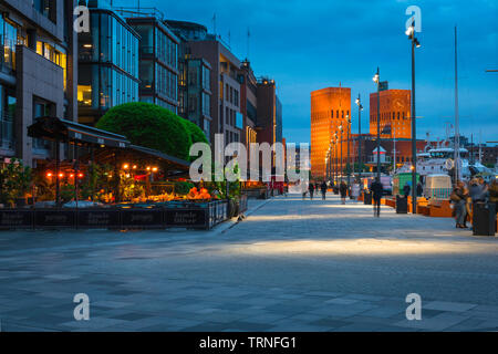 Porto di Oslo, vista di notte del quartiere portuale (Aker Brygge) nel centro di Oslo con il palazzo Comunale (Radhus) nella distanza, Norvegia. Foto Stock