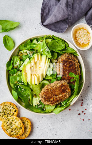 Verde con insalata di avocado, cetriolo e cotolette di lenticchie in una piastra bianca. Foto Stock