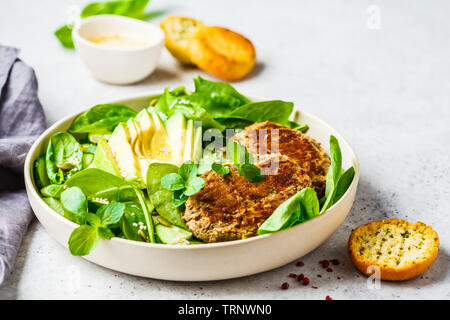 Verde con insalata di avocado, cetriolo e cotolette di lenticchie in una piastra bianca. Foto Stock