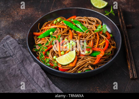 Vegan il grano saraceno soba noodles con verdure in una piastra nera su sfondo scuro. Foto Stock