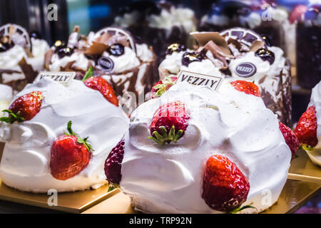 Close-up di torte alla crema di fragole fresche e pasticcini al cioccolato esposti all'interno di una vetrina di panetteria. Foto Stock