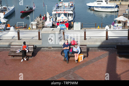 Stanco di turisti e di gente seduta sulle panchine godendosi il caldo sole su una soleggiata giornata autunnale presso il V & A Waterfront di Città del Capo in Sud Africa Foto Stock