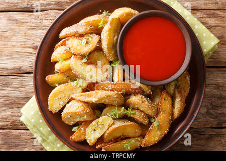 Deliziose patate al forno cunei con parmigiano e origano, serviti con salsa di peperoni close-up su una piastra sul tavolo. Parte superiore orizzontale vista da sopra Foto Stock