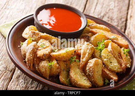 Patate fritte cunei con parmigiano e erbe con salsa di peperoni close-up su una piastra sul tavolo orizzontale. Foto Stock