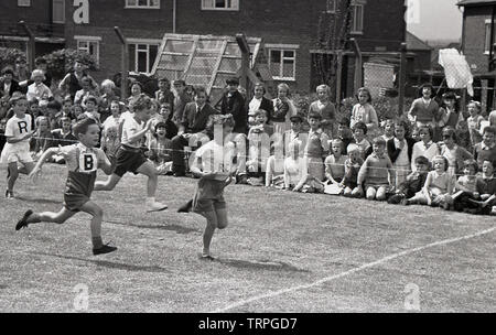 1955, storico, ragazzi in una scuola primaria la giornata dello sport che prendono parte a uno sprint gara di corsa guardato dai loro compagni di scuola seduta dal lato del campo, Inghilterra, Regno Unito. Foto Stock