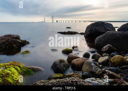 Il ponte ad est del Grande Belt Bridge da Granskoven strand in Danimarca con rocce colorate e il mare in primo piano Foto Stock