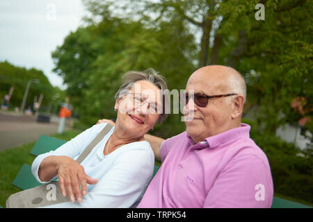 Felice e sano coppia anziana seduta su una panchina insieme al di fuori in bright sole estivo Foto Stock