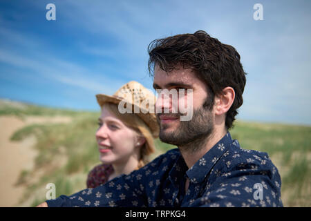 Bella coppia Giovane seduto su una collina sulla sommità di una duna godendo la vista e Ocean Breeze presso la spiaggia di Bright sole estivo Foto Stock