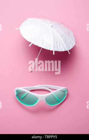 Bianco fotocamera vintage e ombrellone su sfondo rosa. minima arte creativa del concetto. Viaggi e vacanze Foto Stock